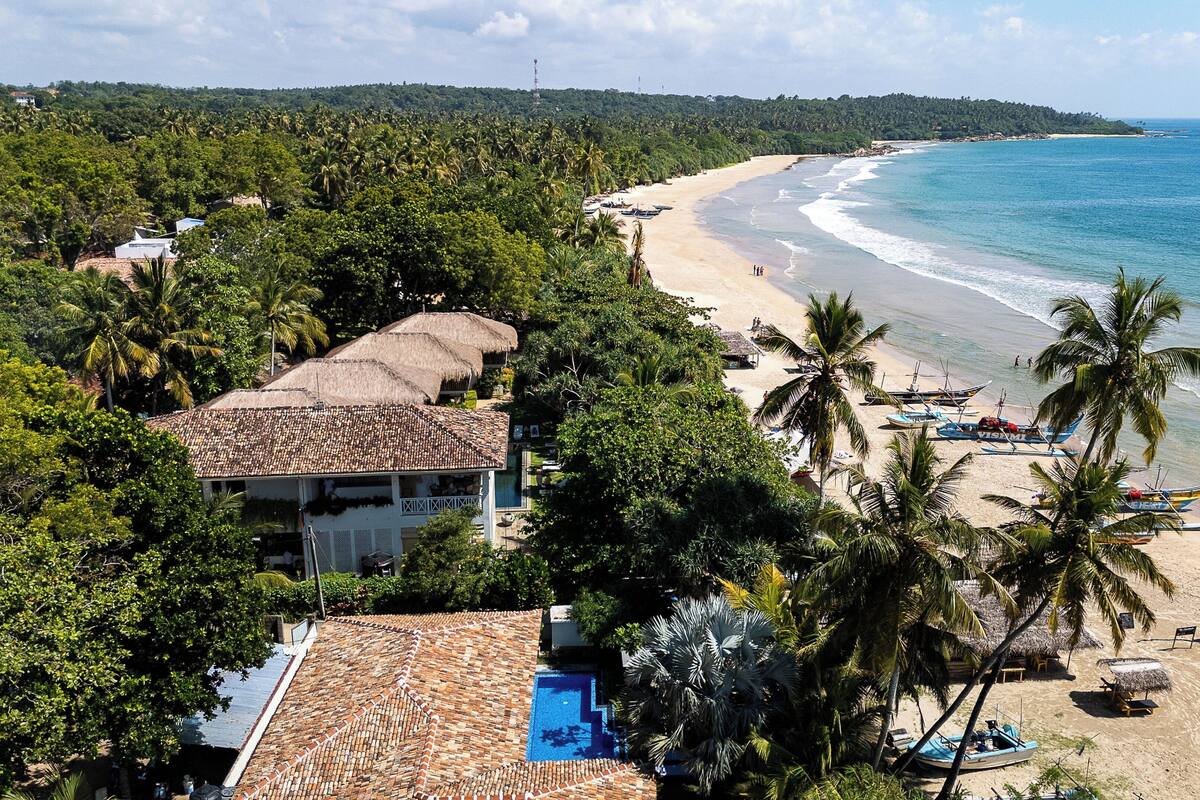 A beach resort with a swimming pool, beachside boats, and palm trees.