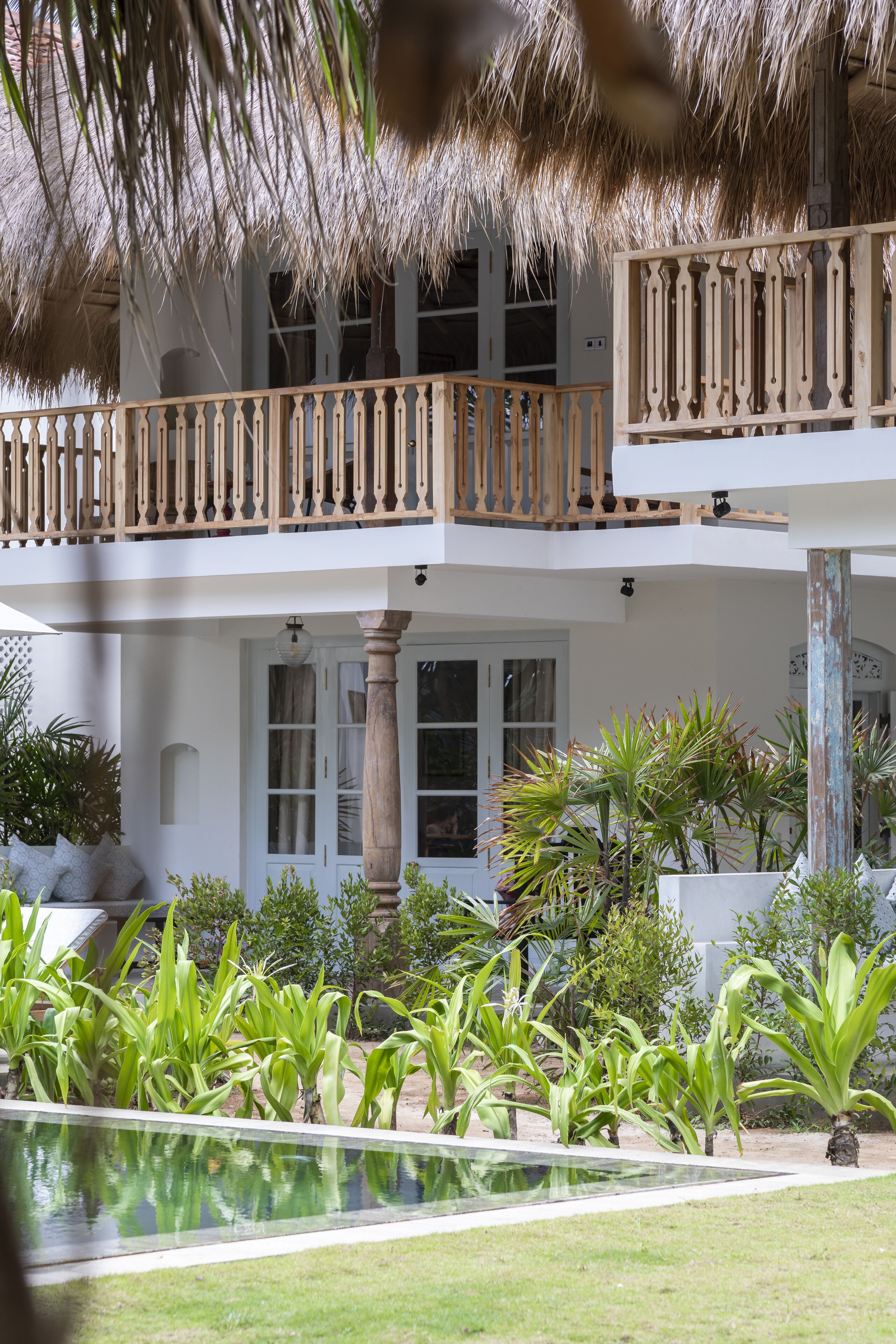 A two-story building with a balcony, a pool, and tropical plants.