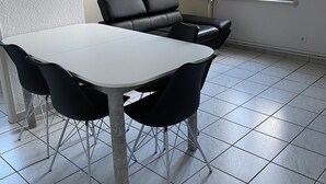 A dining area with a white table and black chairs, a black leather sofa, a tiled floor, and a window with a view of buildings. - Lakefront apartment and walks (Rives)