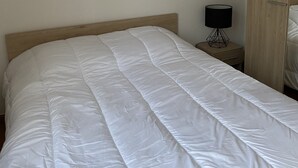 A neatly made bed with a wooden headboard, a bedside table with a lamp, and a wardrobe in a simple, clean room. - Lakefront apartment and walks (Rives)
