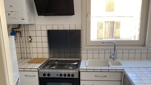 A compact kitchen with a gas stove, oven, white cabinets, a dishwasher, and a window with a view of a building. - Lakefront apartment and walks (Rives)