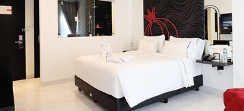 Ein modernes Hotelzimmer mit einem großen Bett, einem Spiegel, einer abstrakten roten Wandkunst und einem kleinen Nachttisch mit Telefon und Wasserflasche.