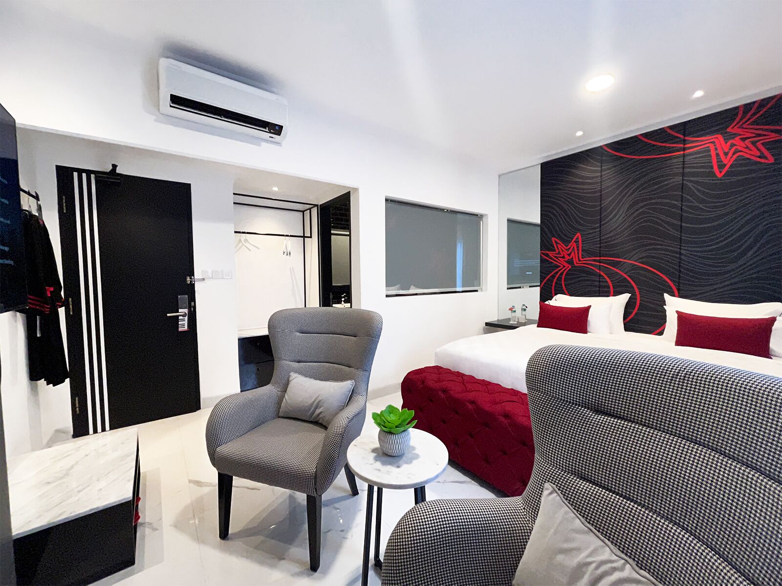 Une chambre d’hôtel moderne avec un lit, un fauteuil gris, une petite table ronde avec une plante et un canapé rouge.