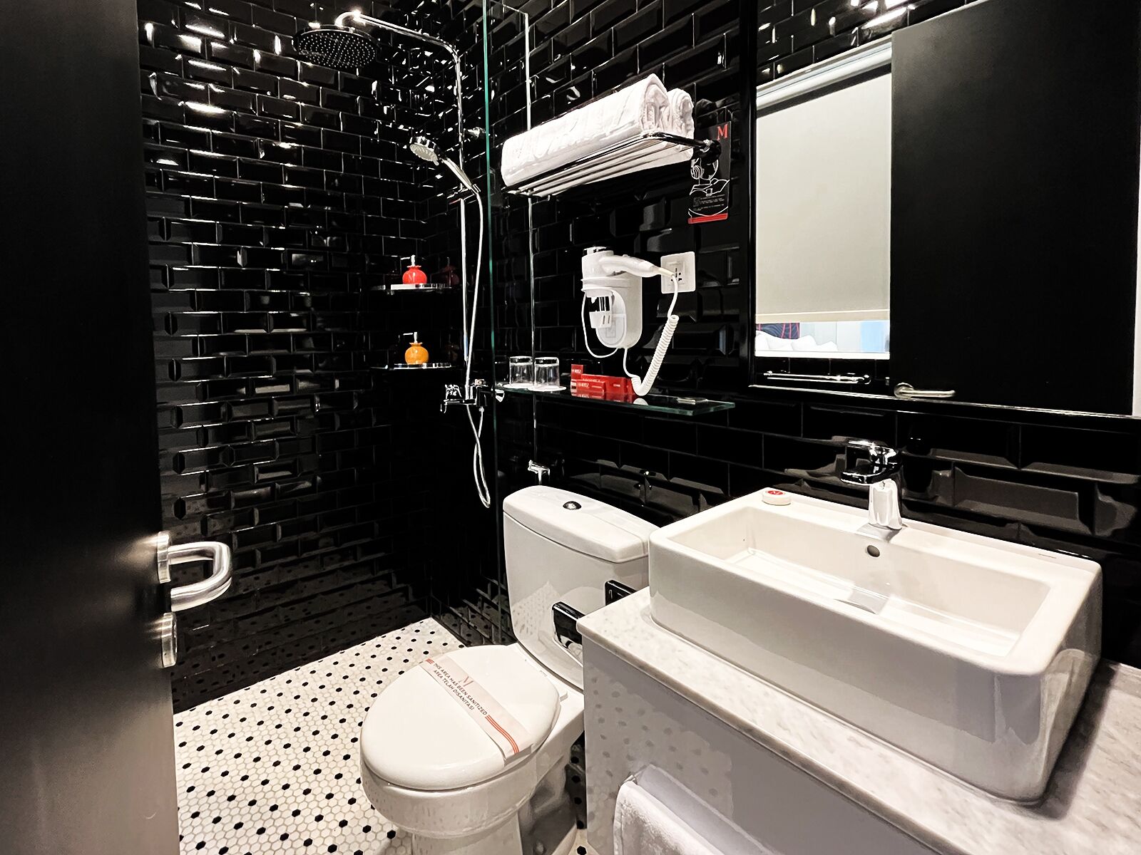 Un baño moderno con pared de azulejos negros, inodoro blanco, lavamanos y ducha.