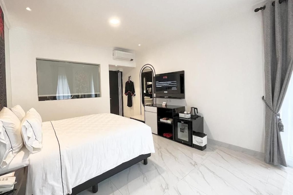 Una moderna camera d'albergo con un letto grande, una TV a schermo piatto, un armadio e un piccolo angolo relax.