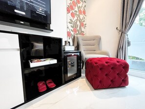 A modern living room with a flat-screen TV, a sofa, a red ottoman, and a decorative wall with a floral pattern. - Moritz Smart Bandung (Bandung)