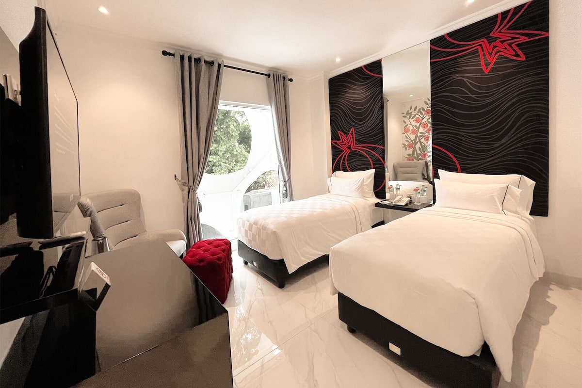 A modern hotel room with two beds, a desk, a chair, and a large window with curtains.