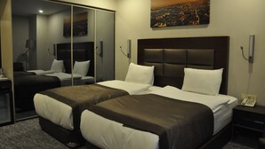 A hotel room with two beds, a large mirror, a painting of a cityscape, and a telephone on the nightstand. - Happy Inn Gebze Hotel (Gebze)