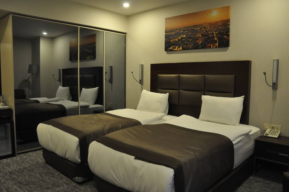 A hotel room with two beds, a large mirror, a painting of a cityscape, and a telephone on the nightstand.