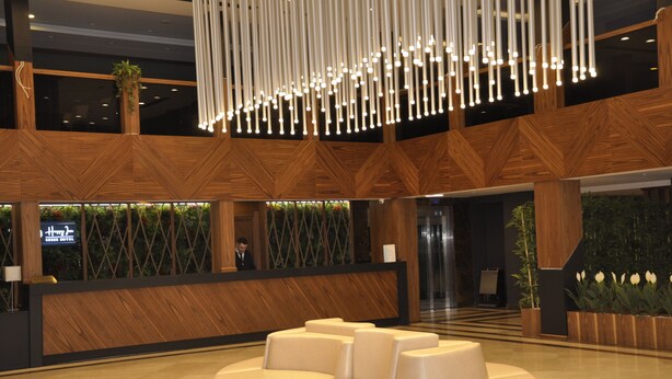 A modern hotel lobby with a reception desk, a seating area, and a decorative light fixture. - Happy Inn Gebze Hotel (Gebze)