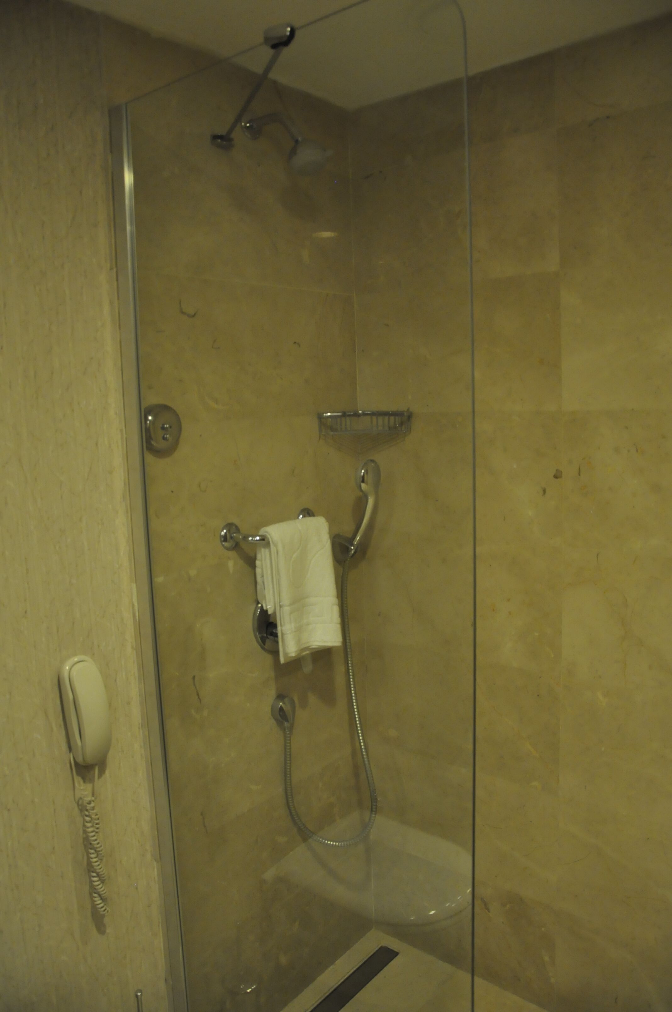 A glass-enclosed shower with a handheld showerhead, a towel rack with a towel, and a telephone on the wall.