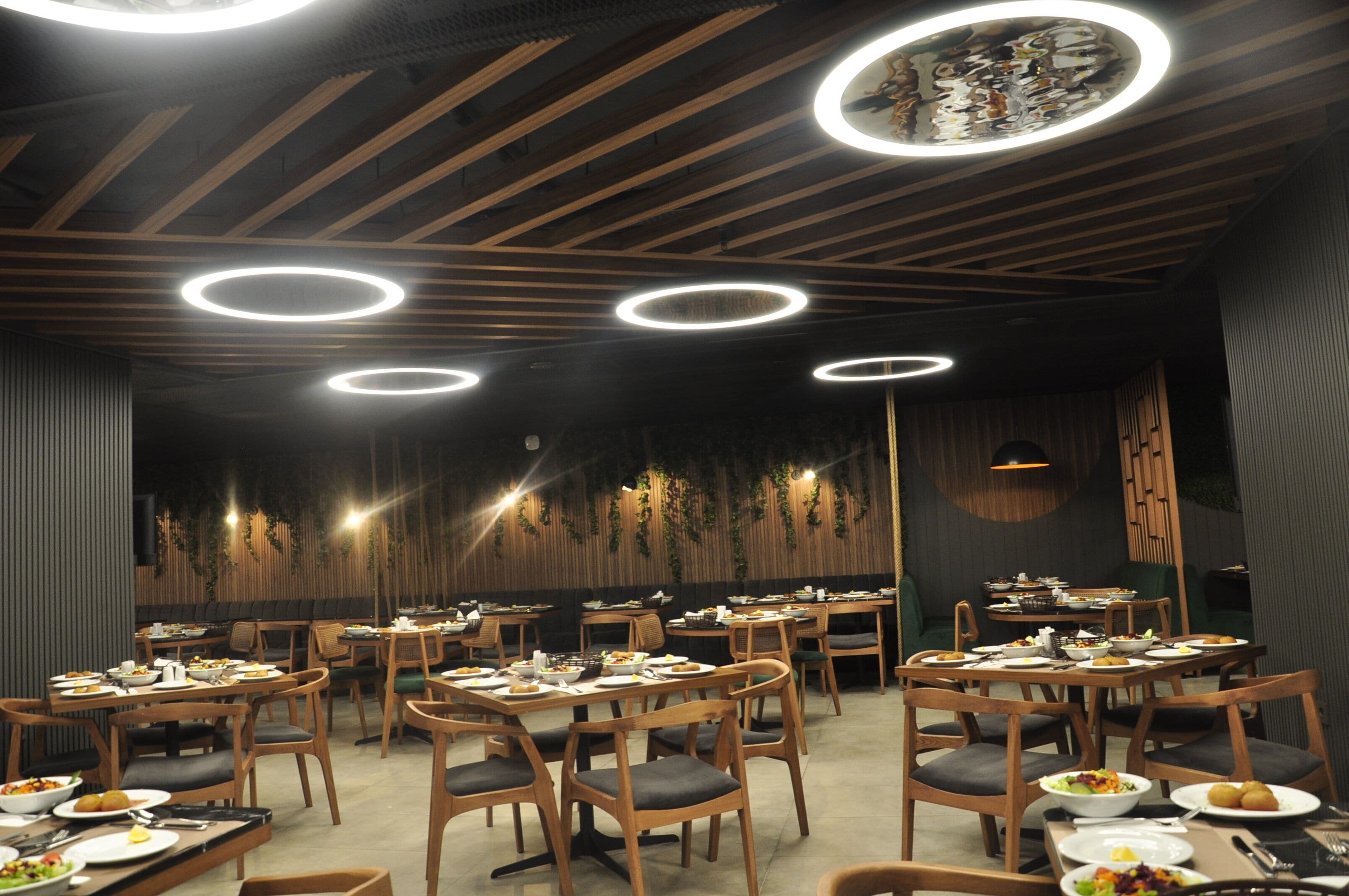 A restaurant with wooden ceiling beams, circular ceiling lights, and tables set with plates and cutlery.