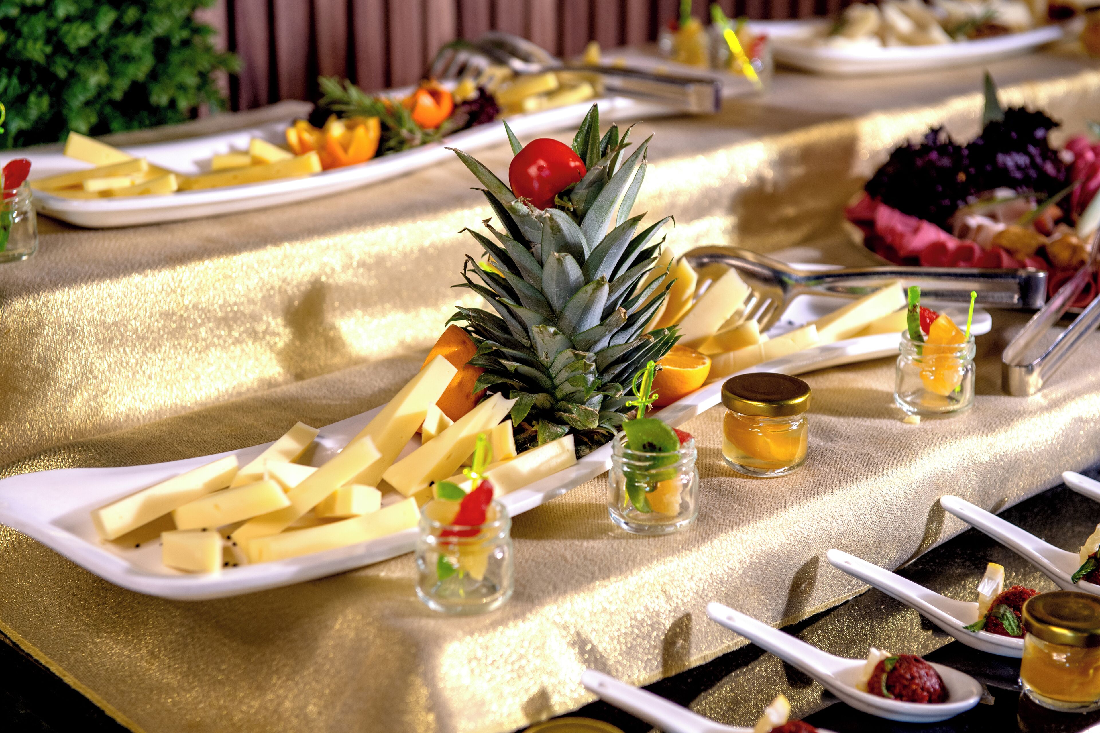 A table set with plates of cheese, pineapple, and small glasses of drink, with a golden tablecloth.