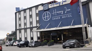 The exterior of the Happy Inn Gebze Hotel with a modern facade, a Shell sign, and several parked cars in front. - Happy Inn Gebze Hotel (Gebze)