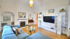 A living room with a sofa, a glass coffee table, a fireplace, a TV, and a chandelier. - Villa Micol: A welcoming two-story independent house located in a picturesque neighborhood of Positano, with Free WI-FI. (Positano)