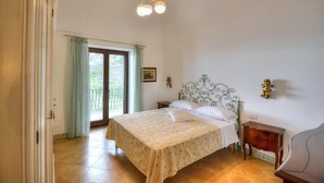 A bedroom with a bed, a nightstand, a chair, a window with curtains, and a decorative ceiling light. - Villa Micol: A welcoming two-story independent house located in a picturesque neighborhood of Positano, with Free WI-FI. (Positano)