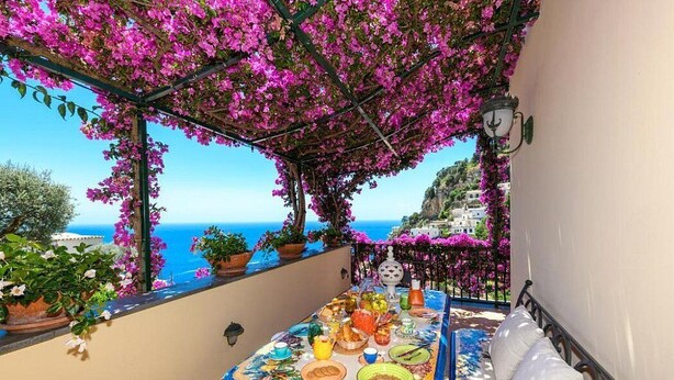 A balcony with a table set for a meal, overlooking a coastal view with buildings and the sea. - Villa Micol: A welcoming two-story independent house located in a picturesque neighborhood of Positano, with Free WI-FI. (Positano)