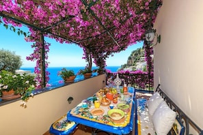 Varanda com mesa posta para refeição, vista para a costa com edifícios e o mar.