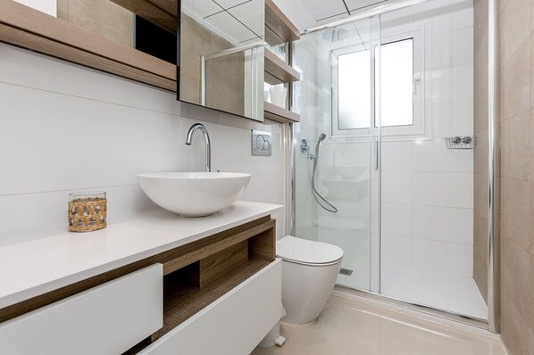 Un bagno moderno con un lavandino bianco, un mobile vanitario in legno, un box doccia in vetro e un water.