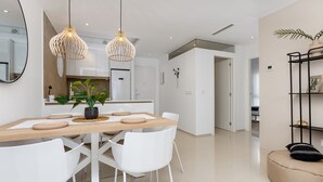 Une cuisine moderne avec des meubles blancs, une table à manger en bois et des luminaires suspendus.