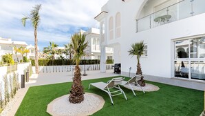 Un patio extérieur moderne avec du gazon synthétique, deux fauteuils de relaxation et des palmiers.