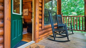Una baita di legno con veranda, una sedia a dondolo e un tappetino d'ingresso.