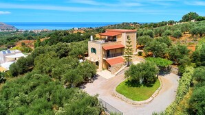 Una casa in pietra a due piani con tetto rosso, immersa nel verde e con vista mare.