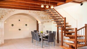 Zona pranzo con arco in pietra, una scala in legno e un tavolo imbandito per sei persone.