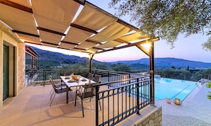 Una terraza con mesa lista para comer, piscina y vistas del paisaje circundante.