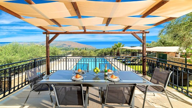 Zona pranzo con tavolo e sedie, una piscina sullo sfondo e vista mare e montagne.