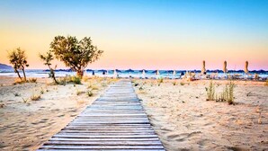 Un sentiero in legno che conduce a una spiaggia con ombrelloni e sedie.