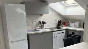 Una cuina compacta amb un fanal i electrodomèstics blancs, a més d'una zona de menjador amb taula i cadires.