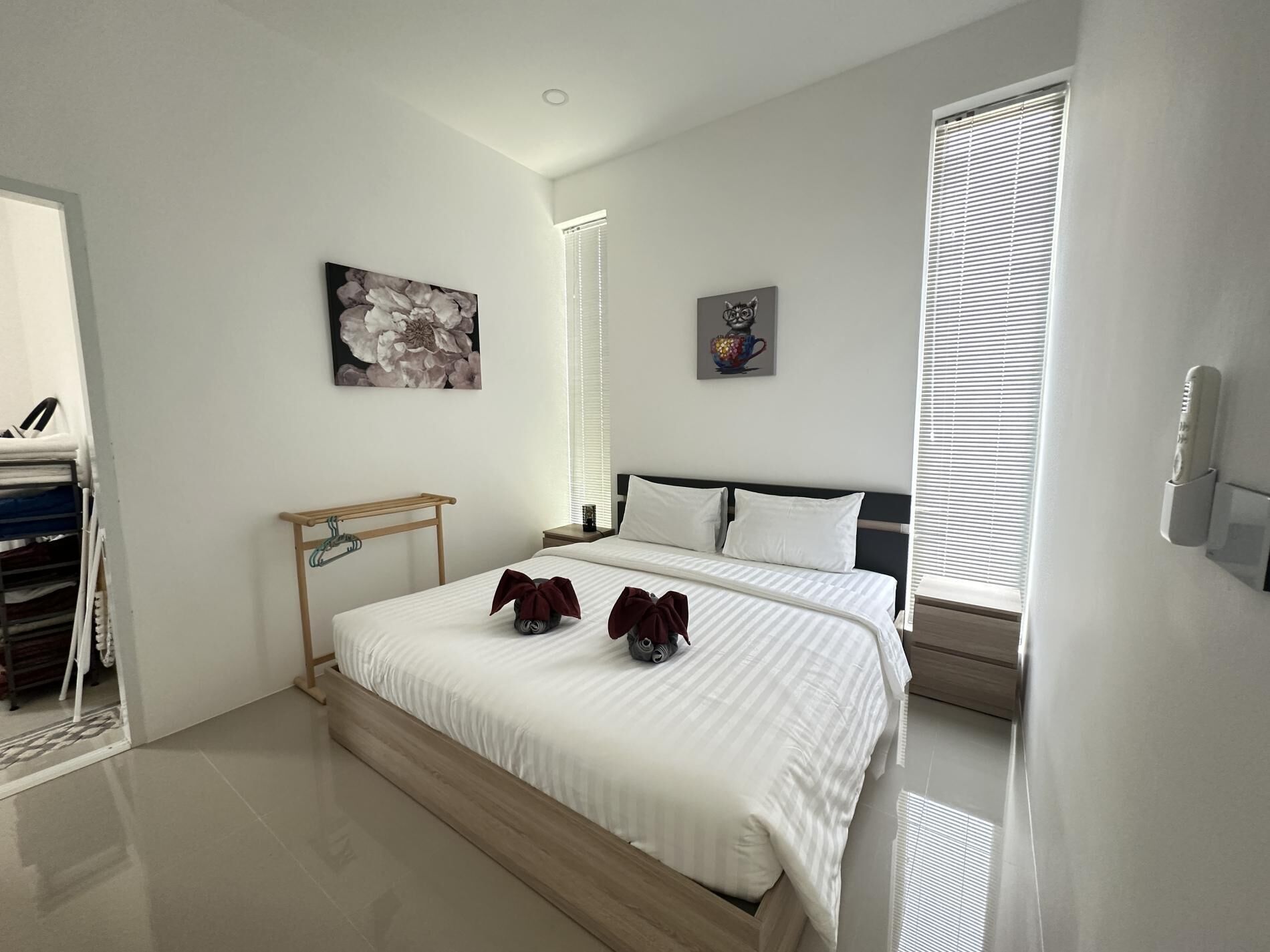 A modern bedroom with a large bed, a wooden bedside table, and two wall-mounted artworks.