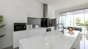 A modern kitchen with white cabinetry, a stainless steel range hood, a microwave, a stove, and a large island with a sink.
