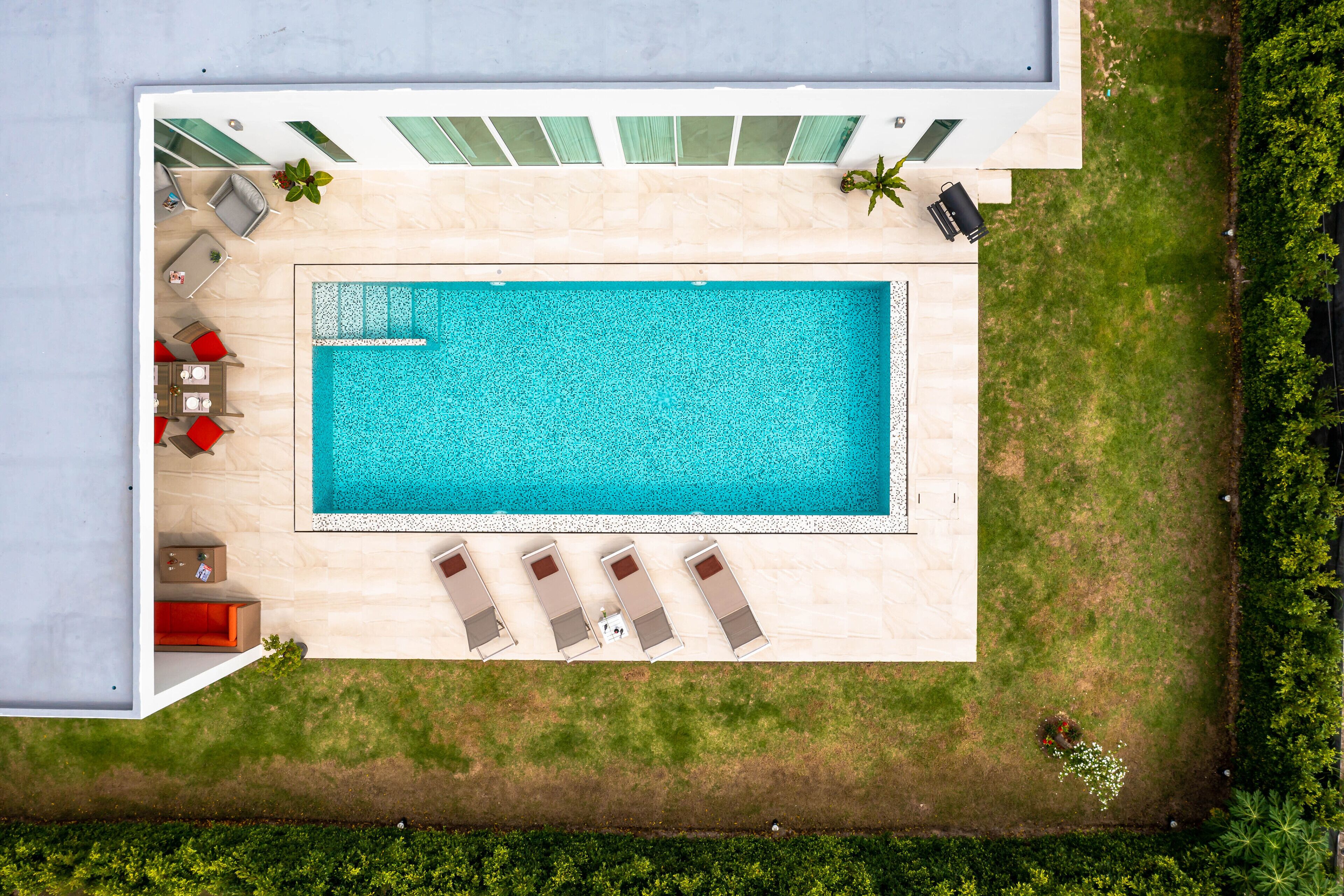 Vista aérea de una casa moderna con una piscina rectangular, un patio con sillas de descanso y una pequeña terraza.