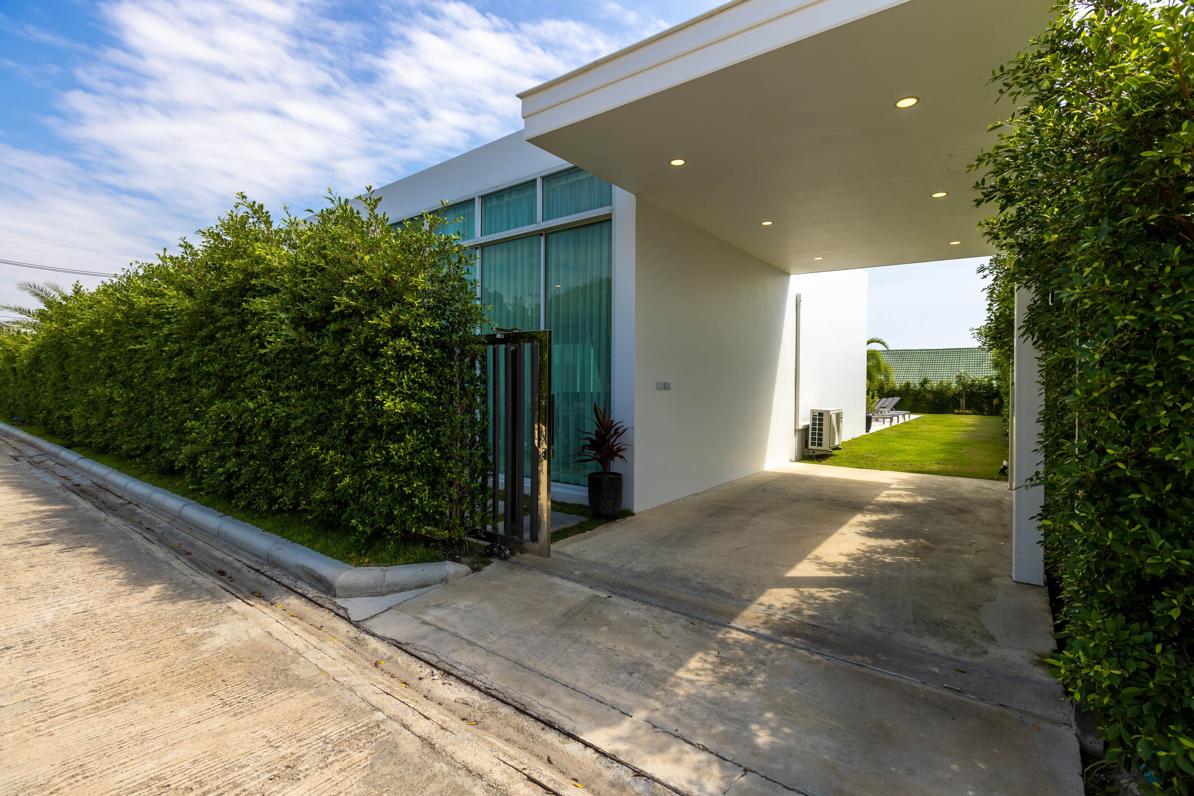 A modern building with a glass facade, a concrete driveway, and well-maintained greenery.