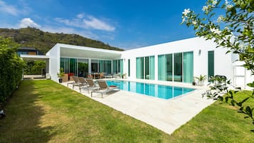 A modern house with a swimming pool, a patio with lounge chairs, and a view of a hill.