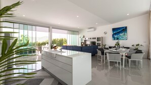A modern kitchen with white cabinetry, a dining area with a table and chairs, and a large window offering a view of greenery outside.