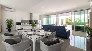 A modern kitchen with white appliances, a dining area with a glass table, and a blue sofa.