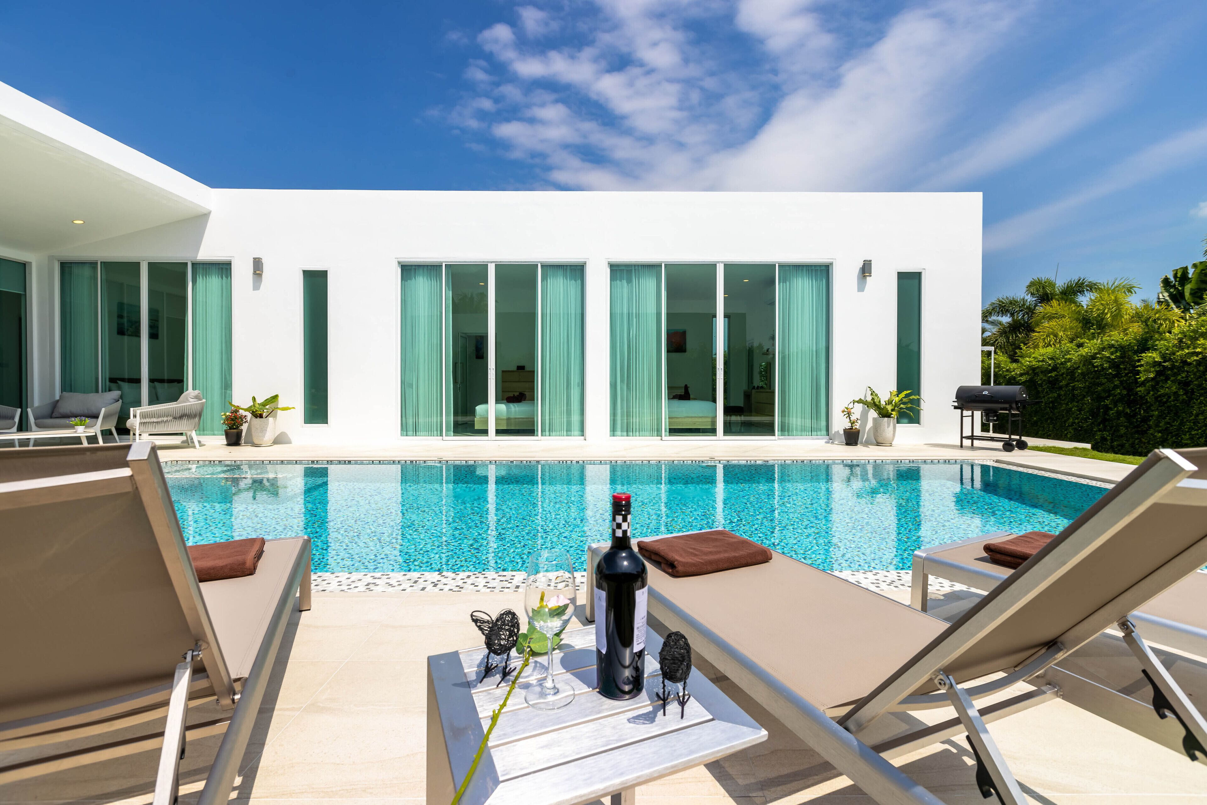A modern poolside area with lounge chairs, a bottle of wine, and a glass of champagne on a table.