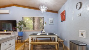 Una cocina con una mesa de comedor, una planta en maceta, un reloj y un cubo de basura.