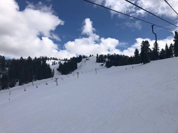 Pista de esquí nevada con telesilla y árboles al fondo.