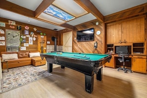 A cozy room with a pool table, wooden cabinets, a television, and a sofa.