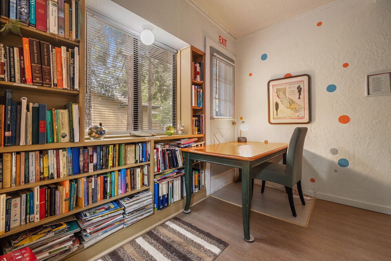Ett rum med en bokhylla, ett bord, en stol och en inramad karta på väggen.
