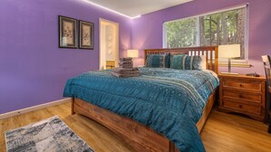 Un dormitorio con cama, mesita de noche, ventana con persianas y una puerta.