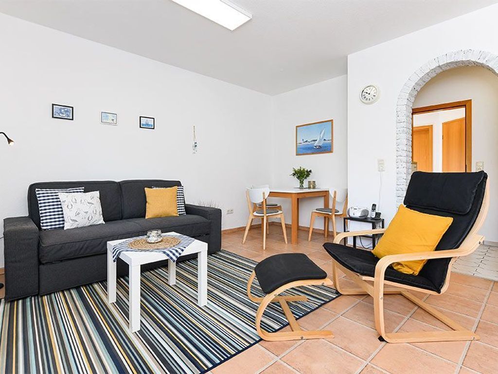 Ett vardagsrum med en soffa, ett soffbord, ett matbord med stolar och en svart stol med en gul kudde. Det finns en klocka på väggen och en inramad tavla ovanför matbordet.