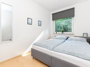 A bedroom with a bed, a window with a view of greenery, and two framed pictures on the wall.
