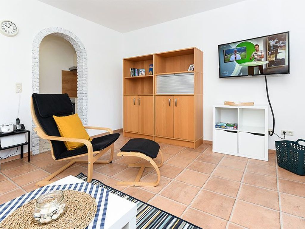 Un salon avec un meuble en bois, un fauteuil noir et jaune, un téléviseur fixé au mur et un sol carrelé.