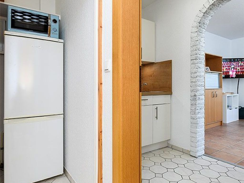 Una cucina compatta con frigorifero bianco, mobili in legno e pavimento in piastrelle esagonali.