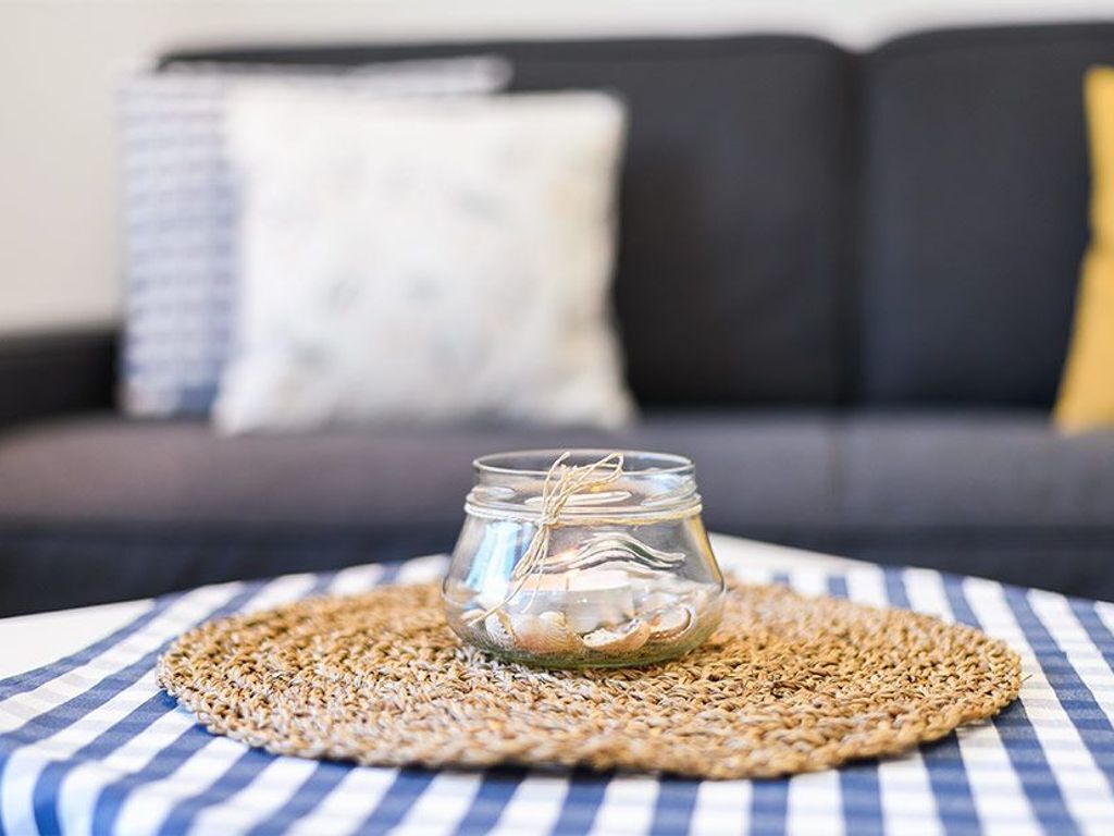 A glass jar with a string, placed on a woven placemat on a checkered tablecloth.